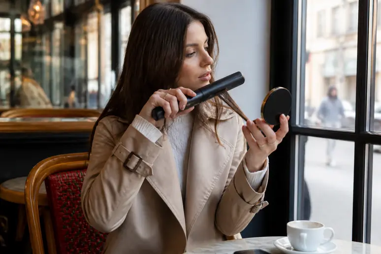 Une jeune femme à Paris utilise un lisseur sans fil pour une retouche rapide dans un café, soulignant la praticité en déplacement.