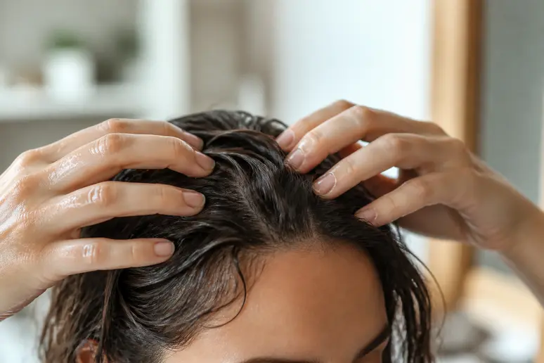Les mains d'une femme effectuent un massage doux du cuir chevelu avec une huile dorée.