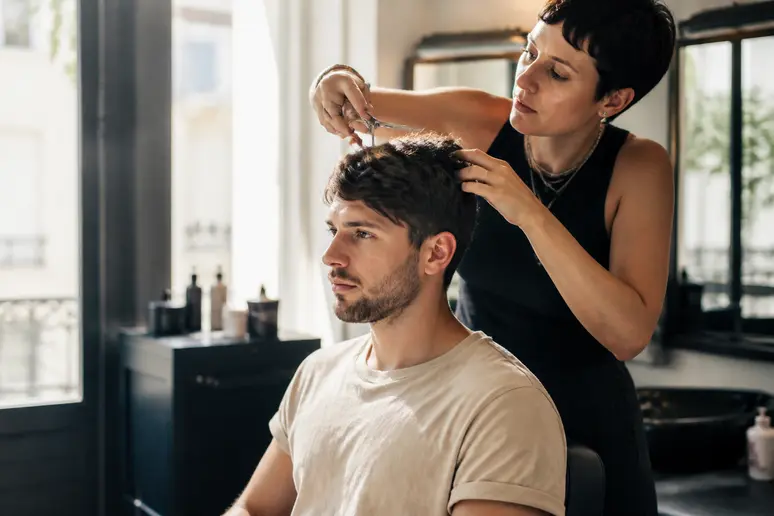 Un coiffeur parisien ajuste une coupe homme avec précision, utilisant des ciseaux dans une lumière naturelle.