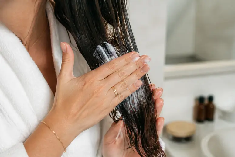 Application méticuleuse d'un masque capillaire sur les longueurs de cheveux humides, dans un souci de soin et de discipline.