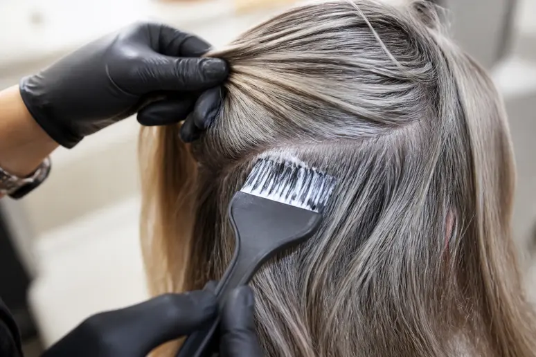 Mains d'une coiffeuse appliquant une patine sur des mèches mélangées à des cheveux gris.