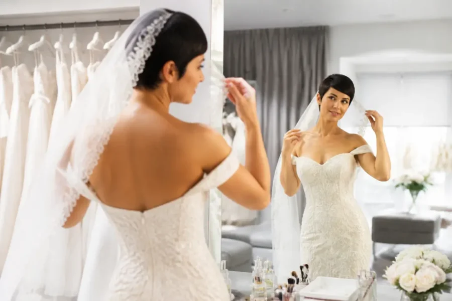 Une mariée avec des cheveux courts ajuste un voile de dentelle pour sa coiffure mariage cheveux courts.