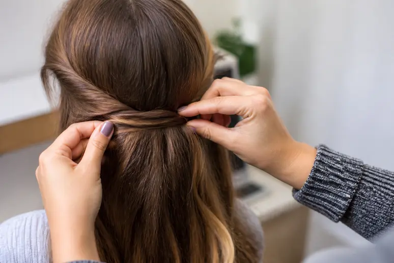 Mains réalisant une demi-queue twistée rapide sur des cheveux longs