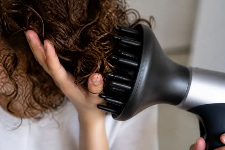 Mains utilisant un diffuseur pour remonter des mèches de cheveux bouclés vers le cuir chevelu.