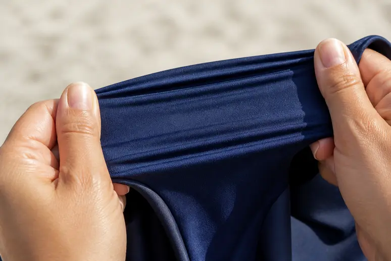 Mains pinçant et relâchant un tissu de maillot de bain pour vérifier son élasticité et sa récupération.