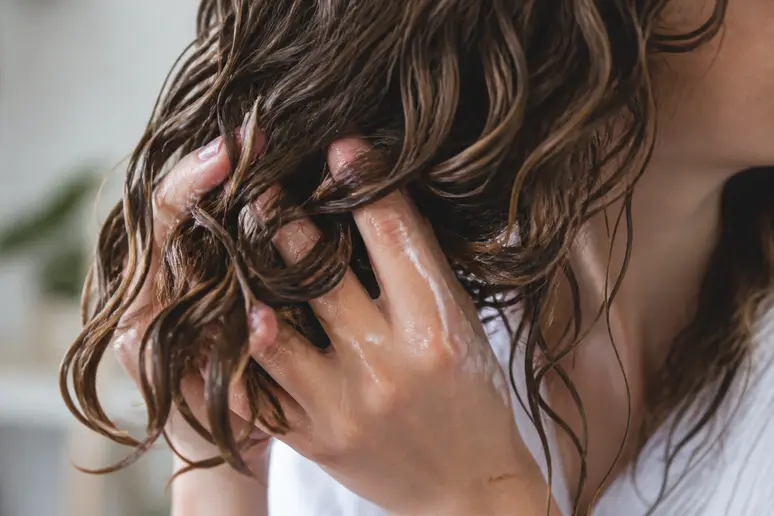 Mains appliquant délicatement une gelée activatrice sur des cheveux ondulés par mouvements de scrunching.
