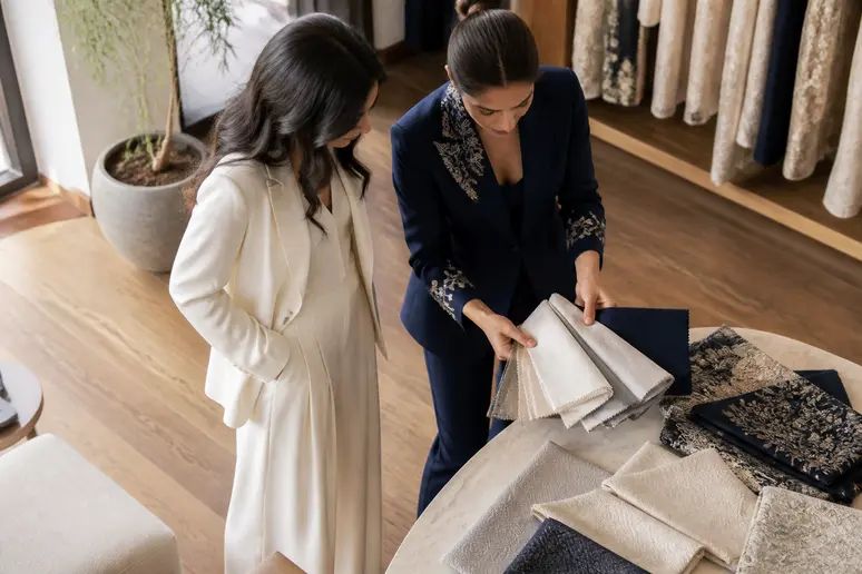 Deux femmes choisissent des tailleurs de mariage, l'une en blanc cassé pour la mariée, l'autre en bleu marine pour une invitée.