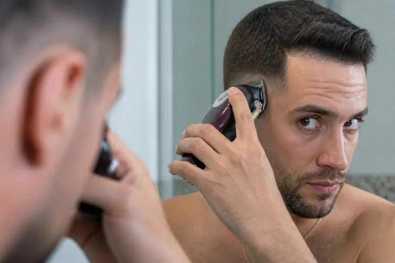 Homme utilisant une tondeuse pour réaliser son dégradé laser à la maison.