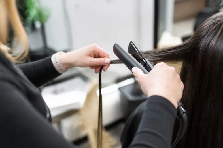 Coiffeur utilisant un fer à lisser sur une mèche lors d'une enzymothérapie