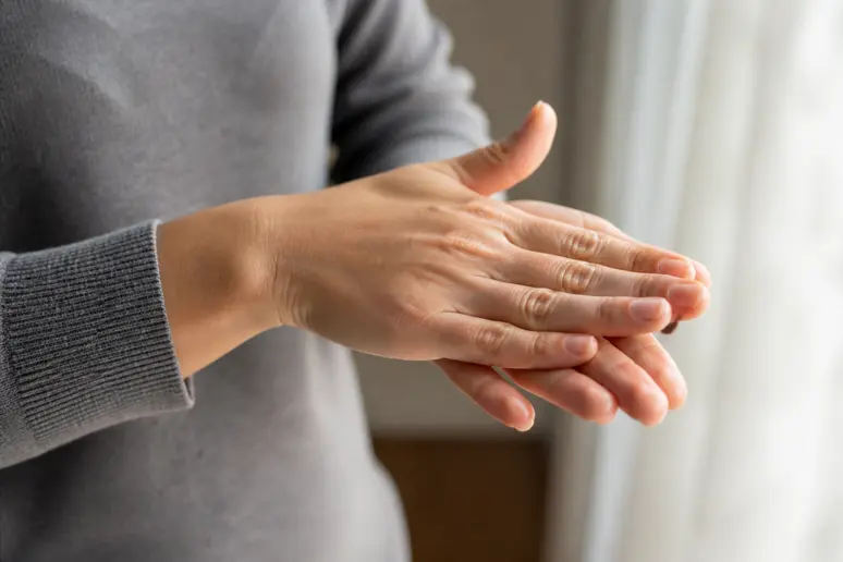 Mains chauffant une goutte d'huile capillaire nourrissante entre les paumes avant application.