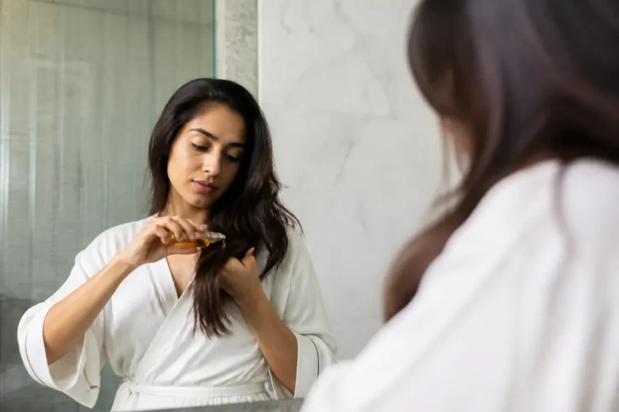 Une femme applique quelques gouttes d'huile mythic oil l'oréal sur ses cheveux propres.