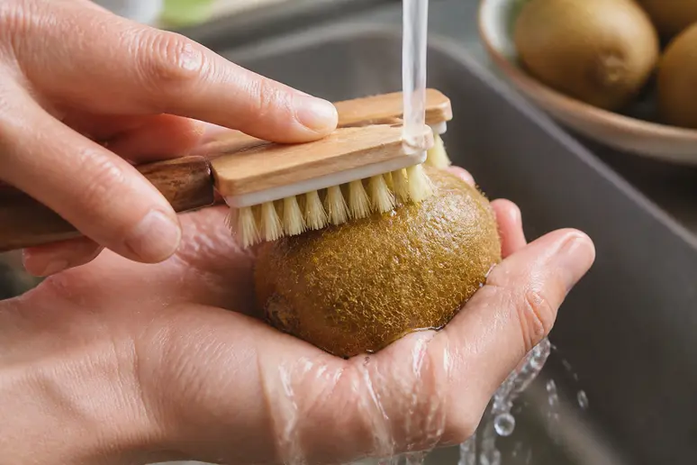 Mains frottant délicatement un kiwi sous l'eau pour nettoyer la peau avant la consommation