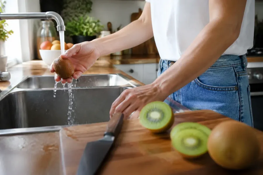 Une personne lave soigneusement un fruit frais avant de manger la peau du kiwi dans sa cuisine.